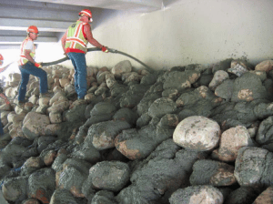 A MnDOT crew applies grout to rounded rocks at a bridge abutment in Milaca in May 2012. The grout cements the rocks together to form matrix riprap, which has shown to be significantly stronger than conventional riprap.