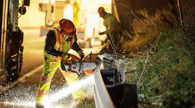 worker on highway using a saw to repair guardrail