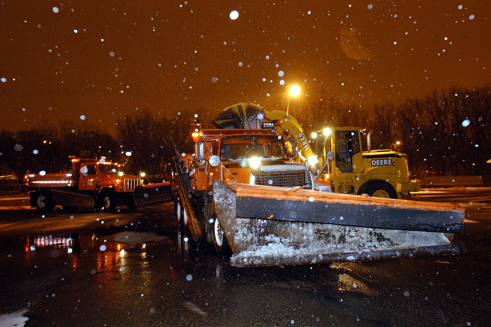 Snowplows and other winter maintenance vehicles clearing roads during a nighttime snowstorm.