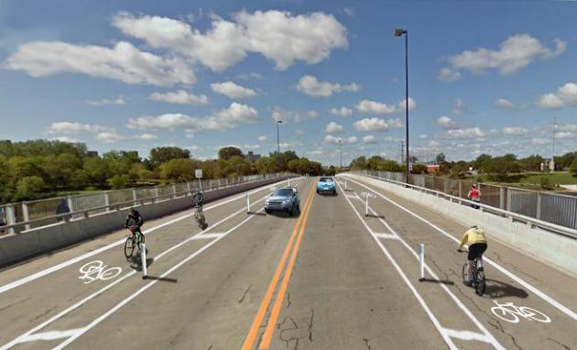 Two lane road with bicycle lanes on both sides of the road with cars on the road and cyclists in the bike lanes.