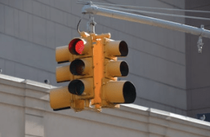 A four-sided traffic signal hangs from a pole over an intersection. The traffic light illuminated on the visible side is red.