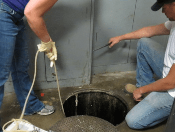A MnDOT maintenance worker and a University of Minnesota employee take wastewater samples from a waste trap at a MnDOT truck-washing facility. 