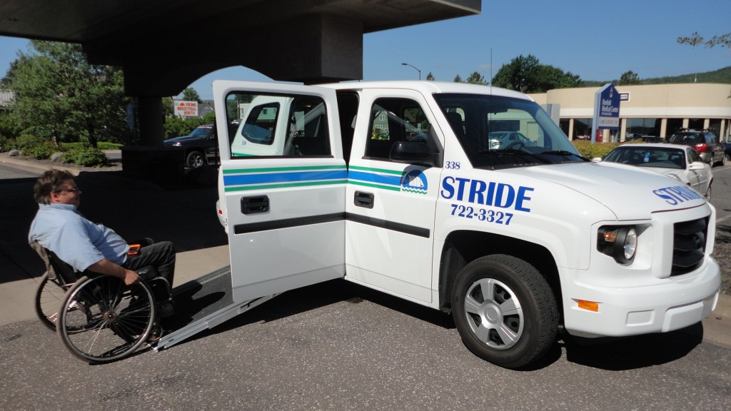 A man in a wheelchair ascends the ramp that has been extended outside a white commercial vehicle.