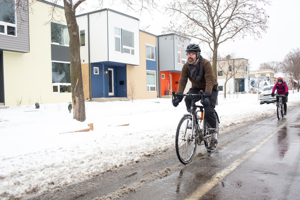 Two cyclists use a bicycle path on an urban street in the snow.