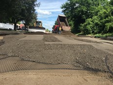 Workers spread a layer of material over the geogrid during road construction.