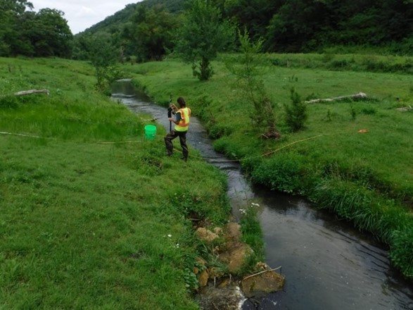 A researcher wearing a safety vest collects data from a stream.