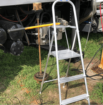 A metal rod inserted into the ground with 4 to 5 feet exposed above ground and a cap on top. Next to the rod are a sledgehammer and a step stool.