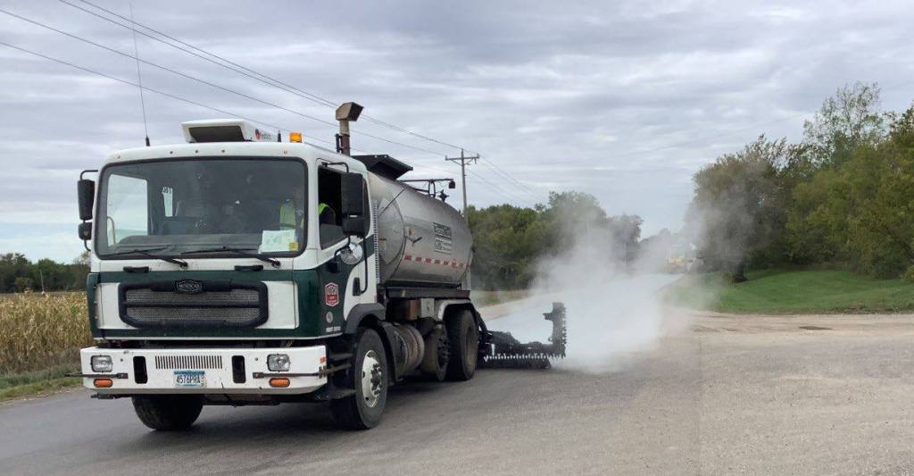 A distributor truck spraying emulsified asphalt onto a road.