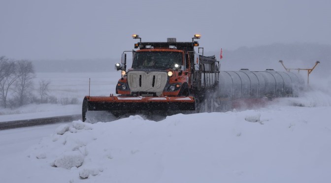 A snowplow driving through deep snow in a rural area.