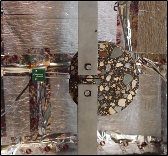A disk-shaped asphalt sample in a tension-testing machine.
