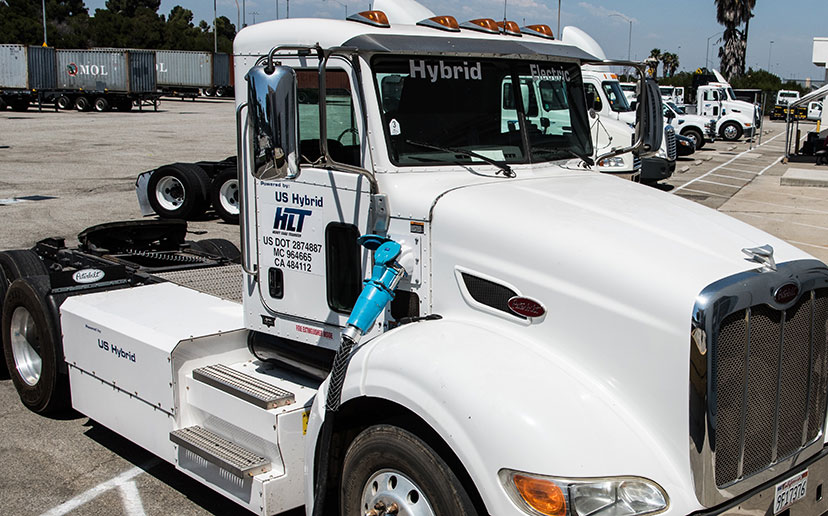 Electric truck chassis and cab in a parking lot with other e-trucks and trailers.