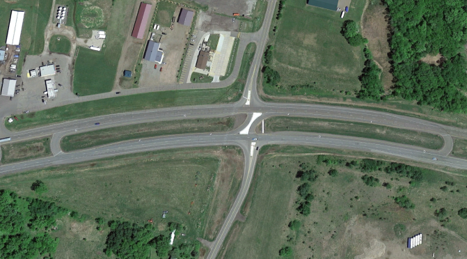 An aerial view of a divided highway intersecting a side road with J-turns on both sides of the side road.