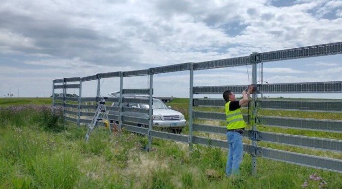 A field worker installs a snow fence with solar panels in place of horizontal fence slats.