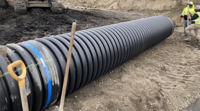 A 3-foot-diameter black corrugated pipe at a road construction site.