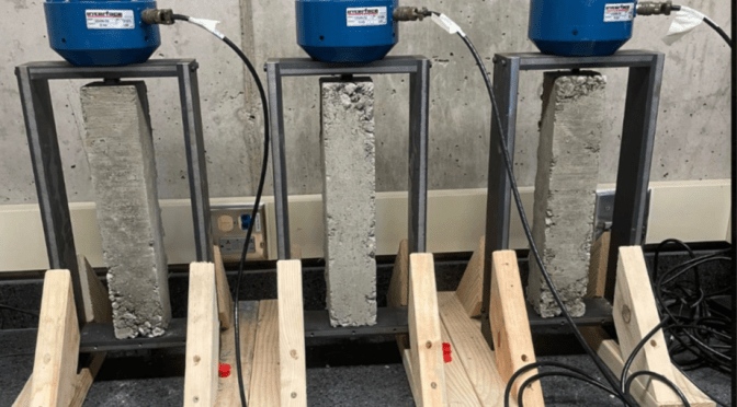 Three restrained shrinkage devices each applying pressure to a concrete prism.