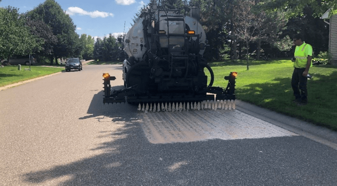 A tanker spraying rejuvenator liquid from a rear dispenser onto a road.