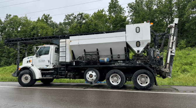 A large white volumetric mixer combines new low slump concrete for bridge overlays.