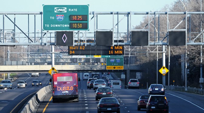 A variety of analog and digital roadway signage is arranged overhead traffic.