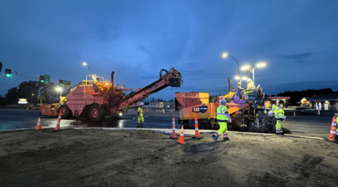 A large material transfer vehicle loads a paving vehicle with asphalt as it applies a pavement layer to the road.