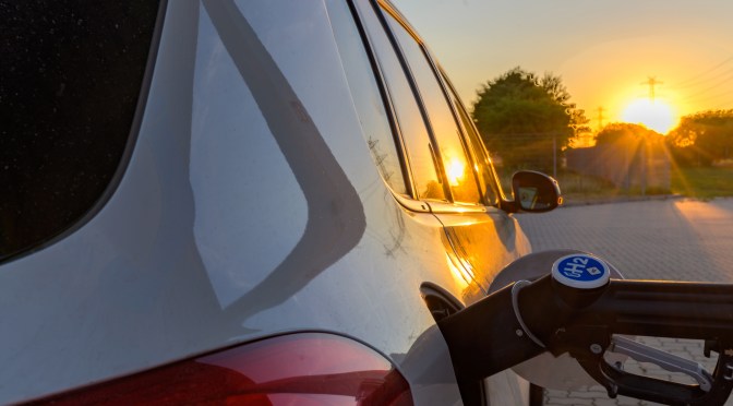 A close up view of a car being fueled up with hydrogen fuel as the sun rises or sets on the horizon.